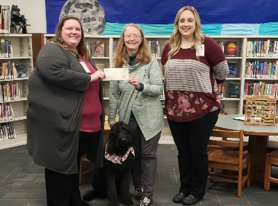 Three people pose with a dog at the library.